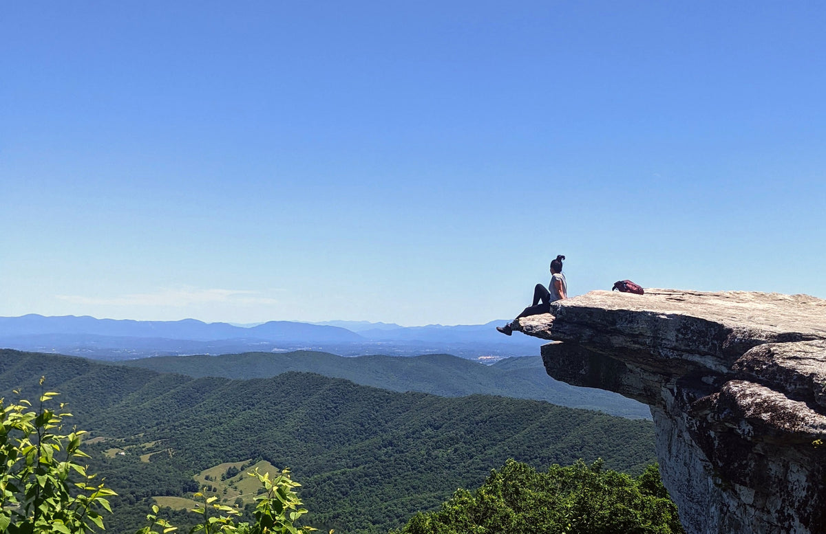Sitting on a cliff edge above forested mountains